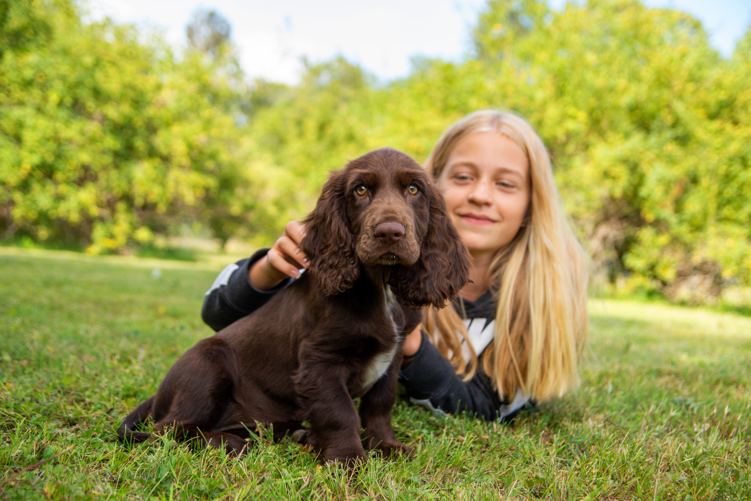 Flicka och hundvalp ute på gräsmatta.